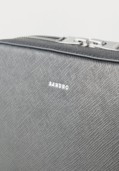 Γκρι δερμάτινο νεσεσέρ με υφή, ασημένιο φερμουάρ και λευκή επωνυμία "SANDRO" στο κέντρο της μπροστινής πλευράς.