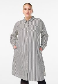 Sukienka koszulowa w czarno-białe paski. Zapięcie na guziki z przodu, kołnierzyk, długie rękawy, boczne kieszenie, sięga do połowy uda. Lekki materiał.