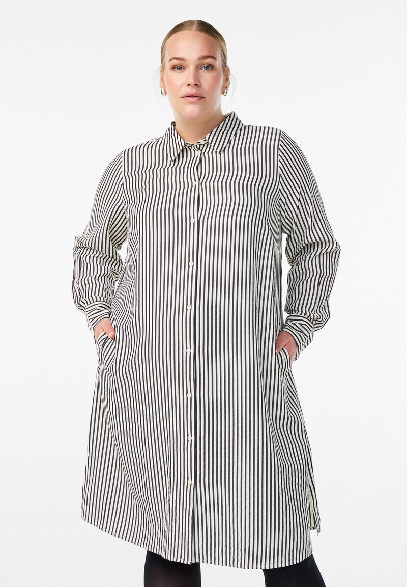 Sukienka koszulowa w czarno-białe paski. Zapięcie na guziki z przodu, kołnierzyk, długie rękawy, boczne kieszenie, sięga do połowy uda. Lekki materiał.