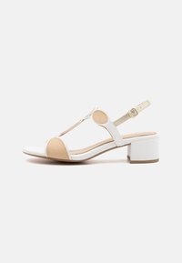 Hvit og beige blokk-heels sandaler med T-stroppdesign, sirkulære detaljer, justerbar ankelstropp og glatt læraktig tekstur.