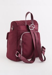 Sac à dos bordeaux au design élégant et rembourré, avec des bretelles réglables, une poignée supérieure et une poche zippée à l'avant. Présente des accents en matériel argenté.