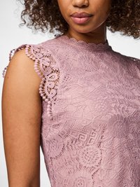 Nærbilde av en kvinne som har på seg en ermeløs mauve blonder topp med blomsterdesign og bølgete kanter på ermer og hals.