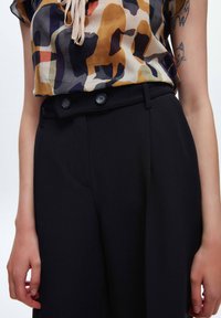 Blus med ett flerfärgat abstrakt mönster, tillverkad av lätt tyg. Svarta byxor med en slät textur och dubbelknäppning.