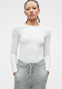 Biała bluzka z długim rękawem połączona z szarymi spodniami dresowymi z prążkowanym pasem i związanym sznurkiem. Gładka tkanina z dopasowanym krojem.