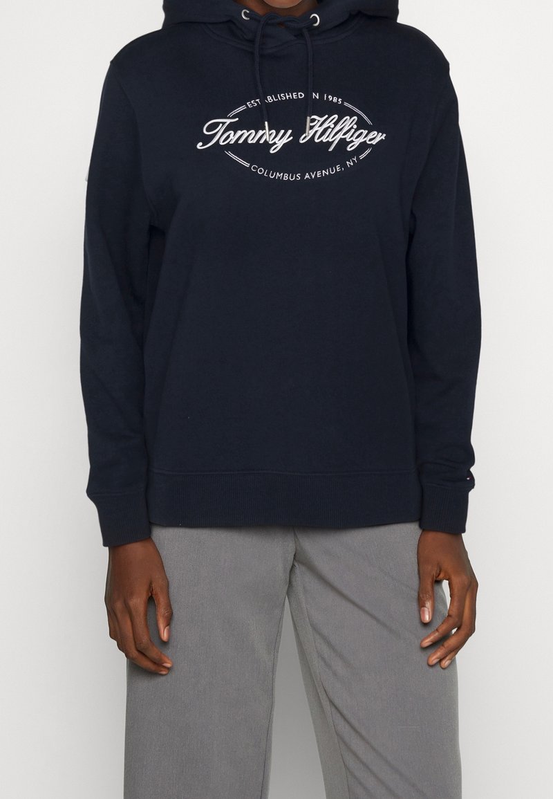 Felpa blu navy con cappuccio regolabile e polsini a costine. Presenta un logo bianco con la scritta "Tommy Hilfiger" sul petto. Tessuto misto cotone.