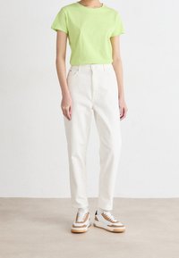 Vihreä puuvillainen pyöreäkauluspaita, valkoiset korkeavyötäröiset farkut ja ruskeilla yksityiskohdilla varustetut lenkkarit, joissa on valkoisia ja mustia yksityiskohtia.