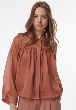 Rustfarbene, oversized Bluse mit lockerem Schnitt, ausgestattet mit einem Button-down-Kragen, einem gerafften Vorderdesign und einem dezenten Glanz in einem leichten Stoff.
