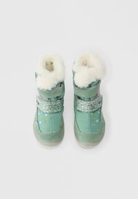 Par de botas de inverno verdes para crianças com borda de pelo branco, tiras brilhantes e pequenos padrões coloridos de corações e pontos na parte superior.