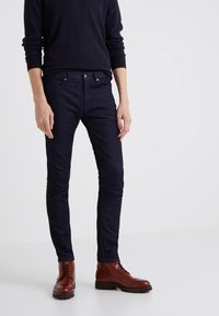 Mörkblå slim-fit jeans i denim, med en klassisk femficksdesign och metallhardware. Kombinerade med bruna snörstövlar.