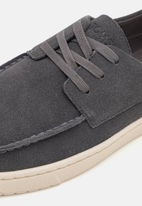 Scarpa in suede grigia con lacci piatti, presenta una suola in gomma beige e cuciture a contrasto. Il design è semplice, senza hardware aggiuntivo.