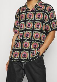Camicia a maniche corte con sfondo nero, decorata da vivaci motivi di bocca e testo nei colori rosa, verde e bianco, realizzata in tessuto leggero.