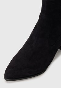 Black suede ankle boot with a pointed toe, smooth texture, and minimal stitching detailing along the sides and a low heel.