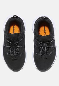Zapatillas deportivas negras con un upper liso, cordones reflectantes y suelas blancas. Presenta una plantilla naranja con el logotipo.
