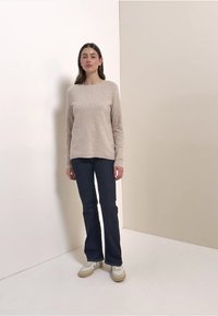 Pull en maille beige clair avec un col rond, porté avec un jean évasé foncé et des baskets blanches. Texture lisse, coupe décontractée.