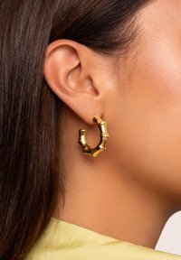 Orecchini a cerchio in oro con un design ispirato al bambù, caratterizzati da una superficie lucida e texture, e da una forma unica e irregolare.