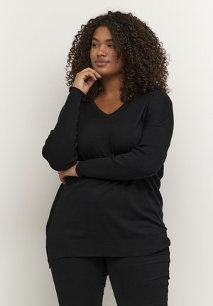 Black knit sweater with a V-neck, ribbed sleeves, and side slits. Worn with black pants, featuring a relaxed fit and smooth texture.
