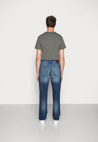 Tajta grå t-shirt i kombination med blå denimjeans som har en blekt tvätt, kontrasterande sömmar och en lappli baktill vid midjan.