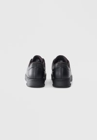 Black athletic shoes with a smooth leather upper, padded collar, and textured rubber sole. Features logo on the heel and perforated accents.