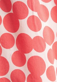 Motivo circolare rosso su tessuto leggero con sfondo bianco, caratterizzato da cerchi di varie dimensioni, creando un design giocoso.