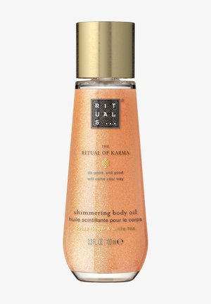 Aceite corporal con brillo en una botella de vidrio transparente con tapa metálica dorada; tono naranja con partículas brillantes; etiqueta con detalles del producto.