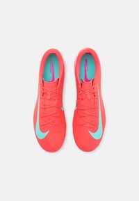 Chaussures de football coral éclatant avec une surface texturée, logo swoosh turquoise et doublure intérieure assortie. Dotées de lacets et d'un design aérodynamique.