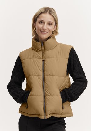 Puffer-vesti khaki värviga, millel on kõrge krae, esi-lukk, küljetaskud ja musta nööpvahvliga varrukad. Sile tekstuur koos tikandmustriga.