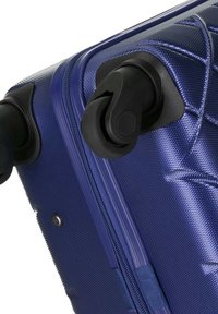 Maleta rígida azul con superficie texturizada, grandes ruedas negras que ruedan suavemente y cierre con cremallera que presenta un sutil patrón geométrico.
