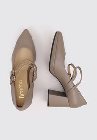 Chaussures Mary Jane en cuir beige avec des pointes effilées, des talons carrés de hauteur intermédiaire et des sangles ajustables. L'intérieur présente un détail de logo. Texture lisse.
