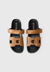 Sandales slides synthétiques marron avec deux larges brides ornées d'œillets ronds dorés et d'un logo découpé, semelles intérieures noires contrastantes.