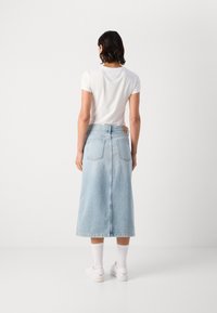 Lys blå denimskjørt med en mid lengde, to baklommer og en jevn finish, kombinert med en hvit t-skjorte og hvite joggesko.