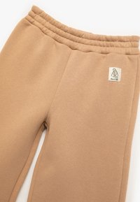 Pantalones de chándal beige hechos de una tela suave, con una cinturilla elástica ribeteada y una pequeña etiqueta en el costado. Textura lisa sin patrones visibles.