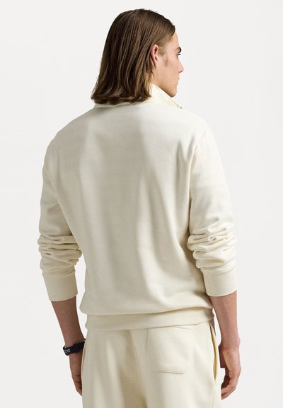 Sweatshirt de un bej deschis, cu guler înalt, manșete acanelate și o croială lejeră. Textură moale a materialului, cu cusături minime și un design casual.