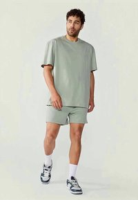 Ljusgrön bomulls t-shirt med korta ärmar, matchad med shorts i samma färg. Outfitten har en avslappnad passform och en mjuk textur, bärs med sportskor.