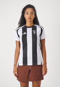 Schwarz-weiße gestreifte Juventus-Trikot mit kurzen Ärmeln, ausgestattet mit dem Adidas-Logo und dem Vereinswappen, kombiniert mit einem braunen Rock.