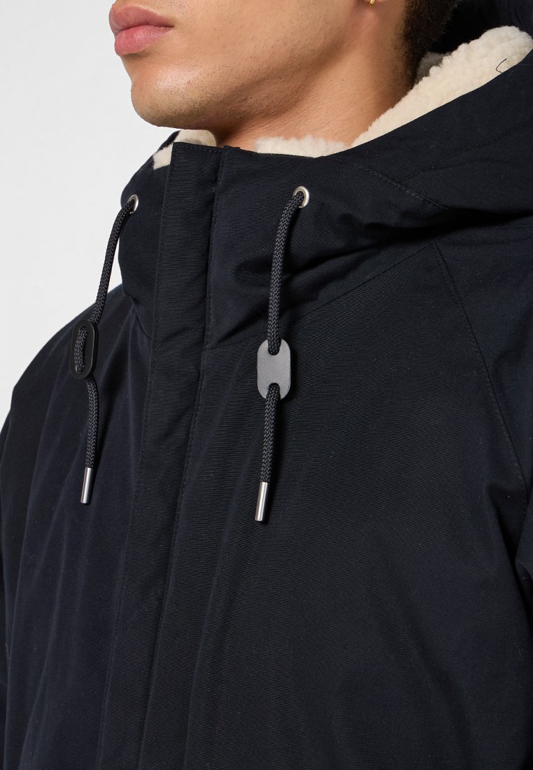 Zwarte hooded jack met een gestructureerde buitenkant, voorzien van een met bont gevoerde kraag, trekkoorden en metallic hardware accenten.
