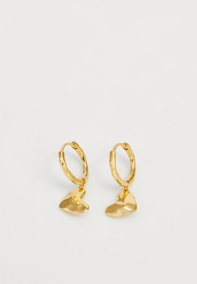 Zlatne naušnice od prstenova s teksturiranim, organski oblikovanim privjeskom. Metal ima sjajnu površinu koja stvara refleksivni efekt.