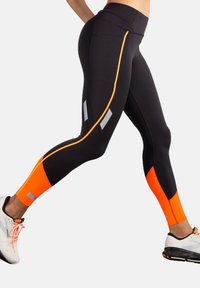 Juodos leggingai su oranžiniais akcentais ir atspindinčiomis detalėmis; tampri medžiaga; suverstomis kulkšnims; skirtos sportiniam naudojimui.
