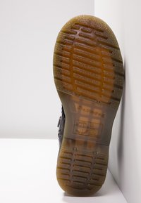 Semelle d'une botte noire avec un dessin de gomme translucide marron, affichant la marque "The Original" et des marquages de résistance à l'huile et à l'acide.