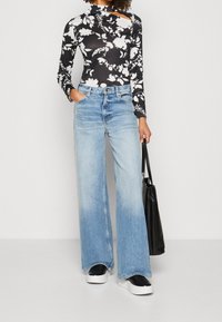 Zwart bloemen lange mouwen bodysuit, licht gewassen wijde jeans, zwarte platform sneakers en een zwarte tote bag. Glad materiaal en een subtiele ombre-effect.