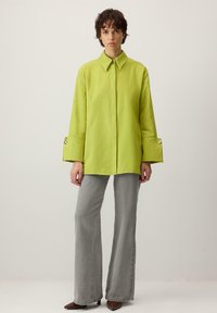 Laimeroheline liibuv särk terava kraega, pikkade varrukate ja nööbitavate mansettidega, koos hallide laiade pükste ja pruunide kontsakingadega.