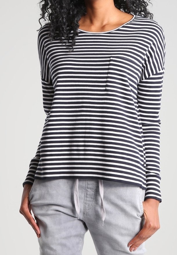 Femme portant un tee-shirt à manches longues à rayures horizontales noires et blanches avec une petite poche sur la poitrine et un pantalon gris clair à cordon de serrage.