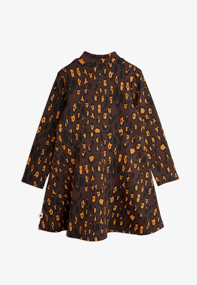 Ruda suknelė ilgomis rankovėmis, su viso paviršiaus leopardų raštu juoda ir oranžine spalvomis. Paprastas dizainas su šiek tiek išplatinta sijonu.