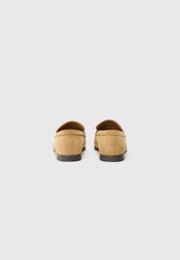 Jasnopopielate zamszowe loafersy z niskim obcasem, okrągłym noskiem i ozdobnym przeszyciem wokół dekoltu. Gładka tekstura i minimalistyczny design.