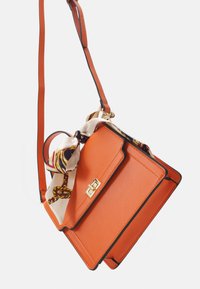 Sac à main en cuir orange au design structuré, avec une bordure noire contrastante et un foulard en soie à motifs noué à la poignée.