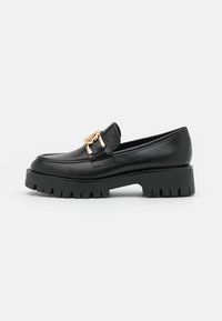 Mocassins en cuir noir avec une semelle plateforme noire épaisse, ornés d'une boucle dorée sur le dessus. Texture lisse et design classique.