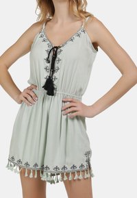 Romper verde claro de tejido suave con bordado floral negro, cinturilla con cordón y flecos a lo largo del dobladillo.