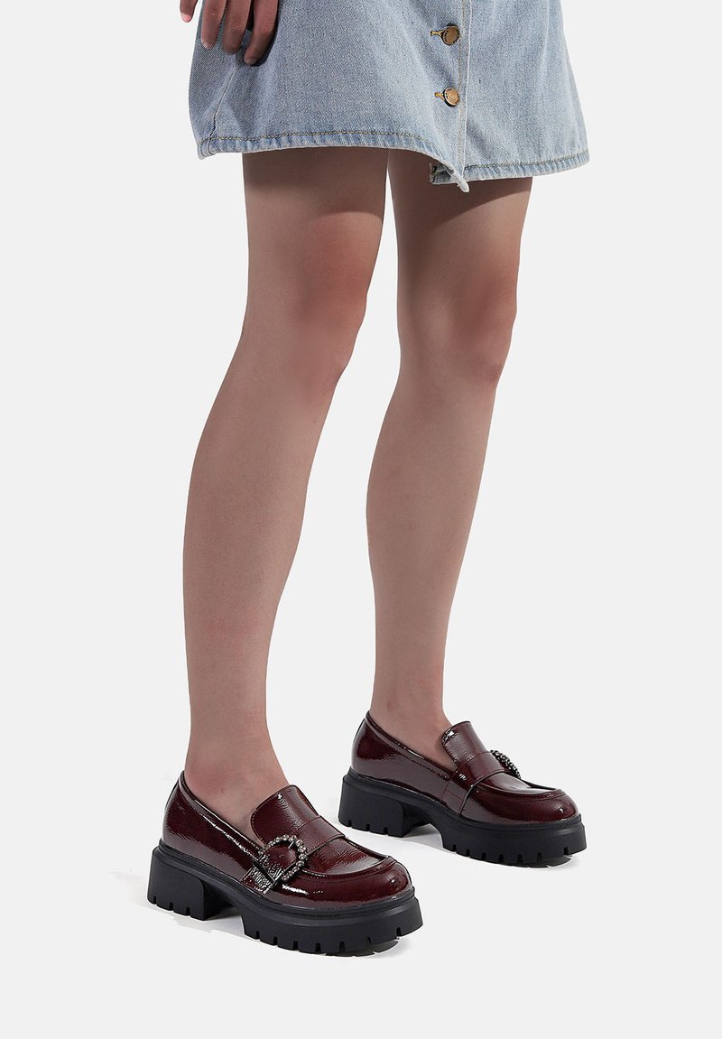Mocassini in pelle verniciata bordeaux con suole nere spesse, dotati di una fibbia decorativa e di una finitura liscia e lucida.