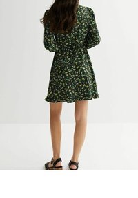 Zwart bloemenjurk met een aansluitende taille, lange mouwen en een gerimpelde zoom, gemaakt van lichtgewicht stof met groene en gele accenten.