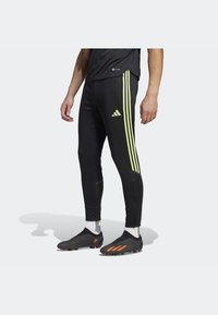 Černé sportovní legíny s třemi svislými fluorescenčními žlutými pruhy a logem. Vyrobené z pružného, lehkého materiálu s zipy u kotníků.