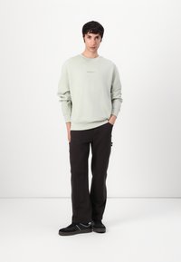 Lysegrøn, struktureret sweatshirt med rund hals, parret med mørke cargo-bukser og sorte sneakers med grå detaljer.